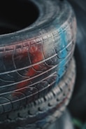 A close-up view of an old tire with distinct tread patterns, partially covered in dust and featuring patches of red and blue paint.