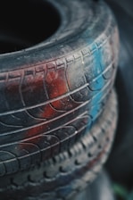A close-up view of an old tire with distinct tread patterns, partially covered in dust and featuring patches of red and blue paint.