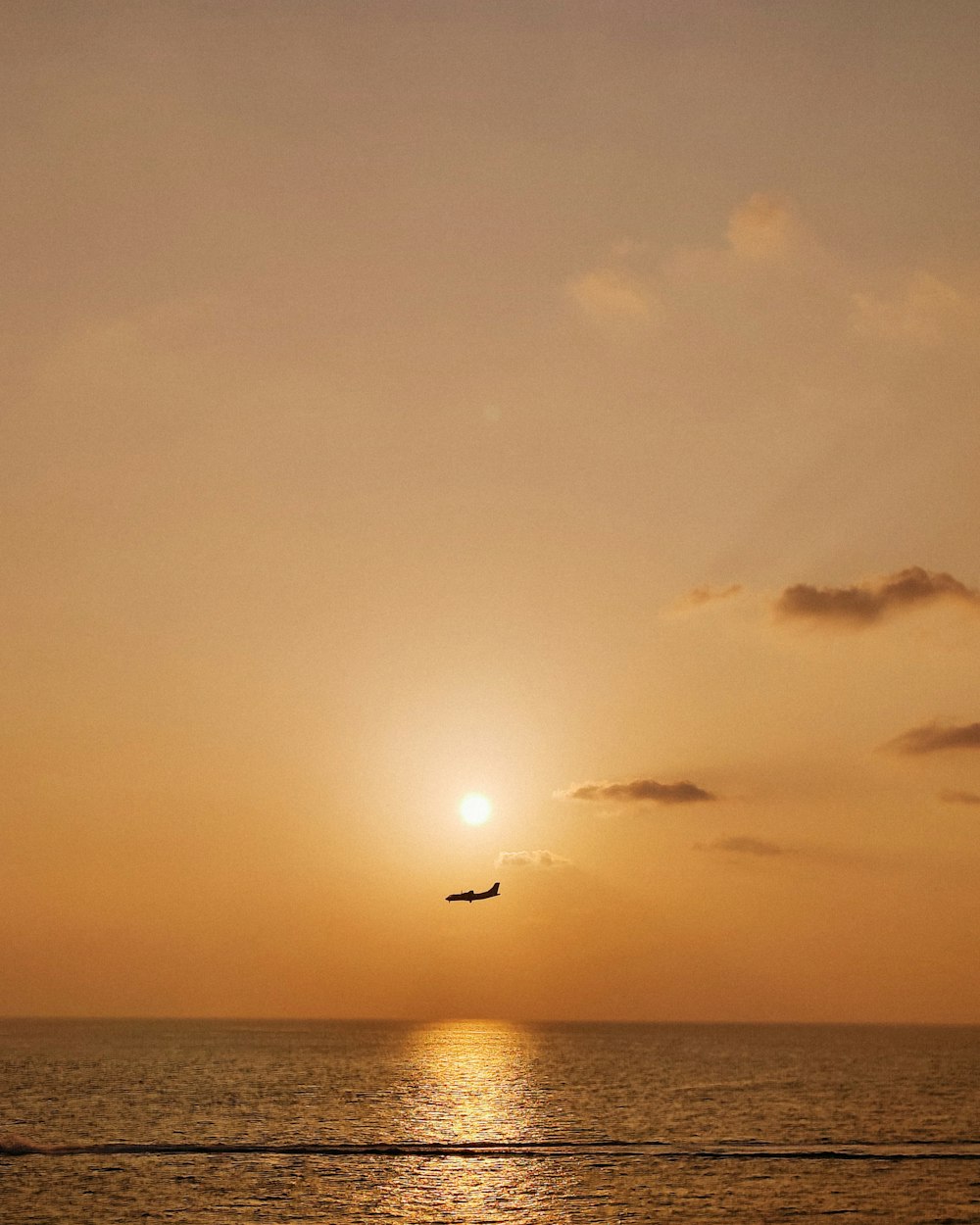 a plane flying over the ocean at sunset
