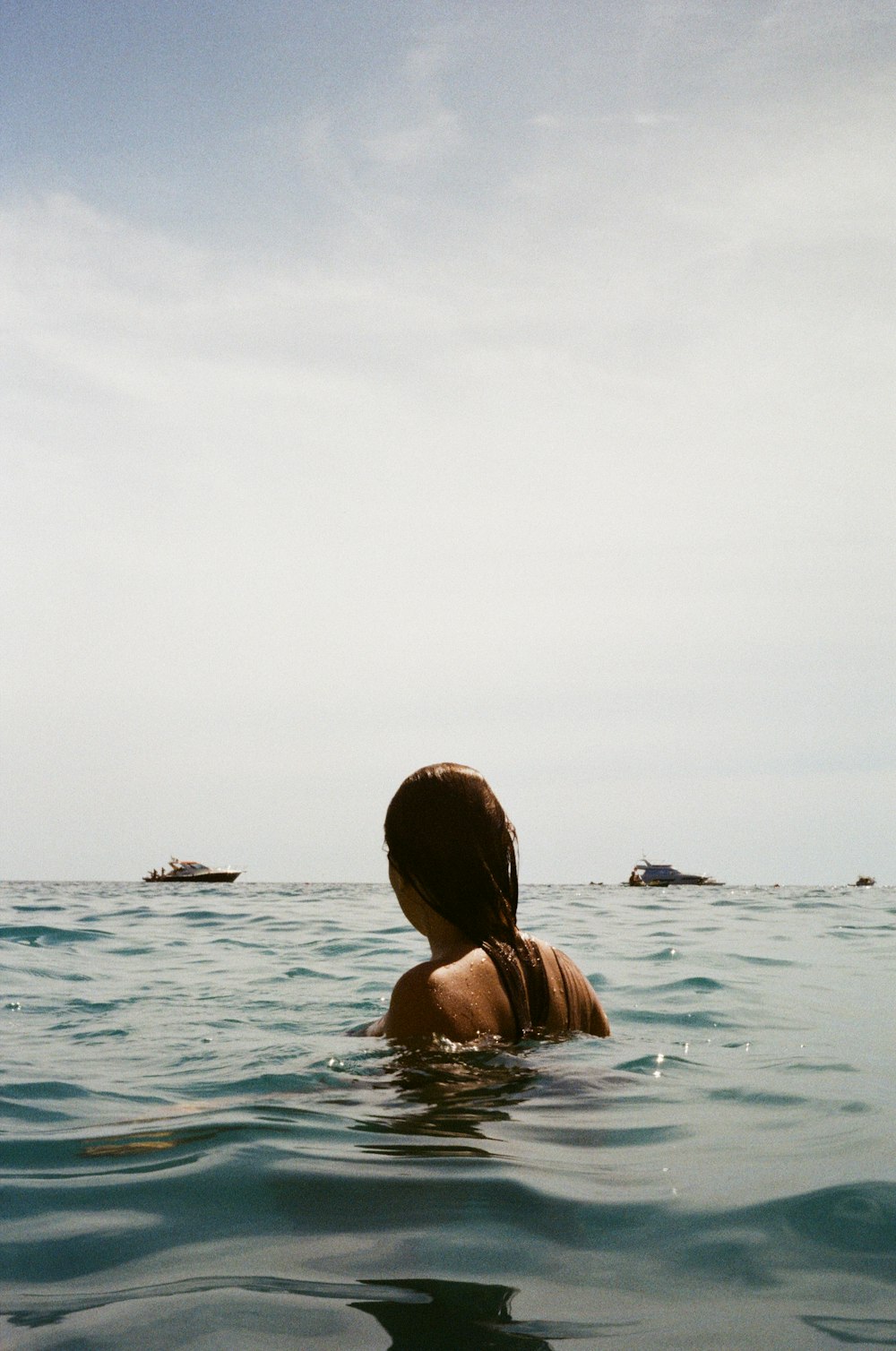 a woman swimming in the ocean with boats in the background