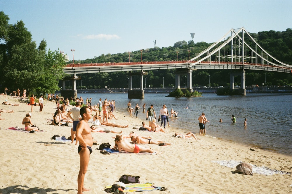 a group of people on a beach near a bridge