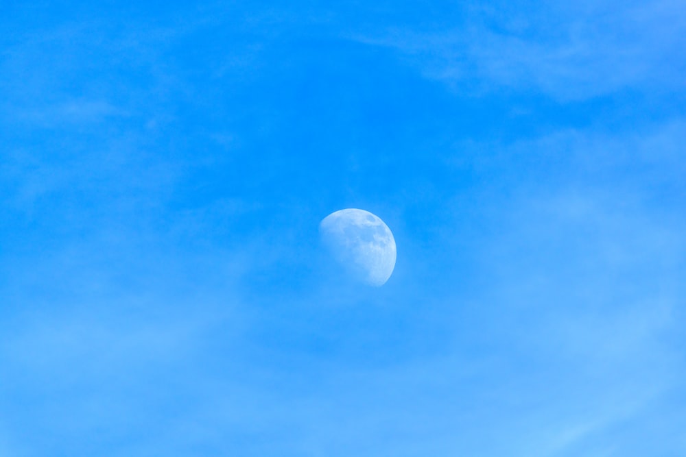 the moon is in the blue sky with a few clouds