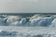 Large ocean waves crash against each other, creating a dynamic and powerful scene. The sea appears turbulent with frothy white caps and a deep blue color in the distance.