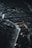An overhead shot of a dark, intricate city model with winding streets and dense urban architecture, highlighted by sparse lighting that creates dramatic contrasts. The image conveys a sense of complexity and order within the labyrinthine arrangement of buildings and pathways.