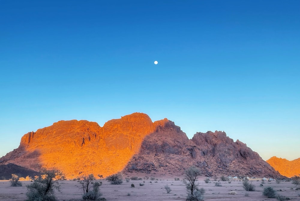 the moon is setting over the mountains in the desert
