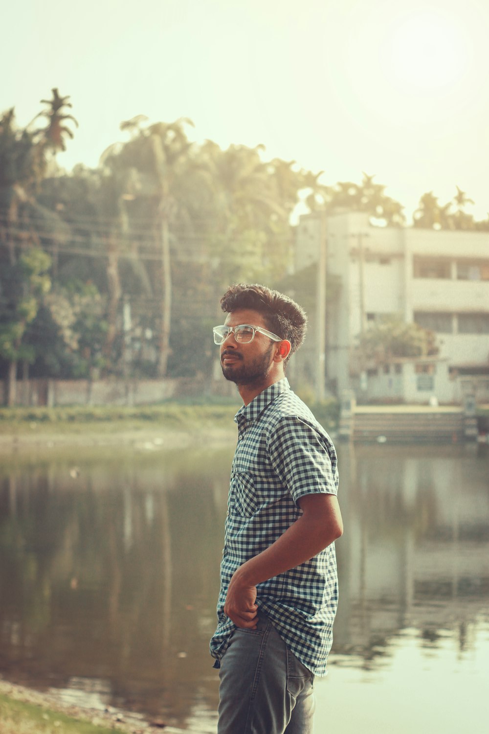 a man wearing glasses standing in front of a body of water