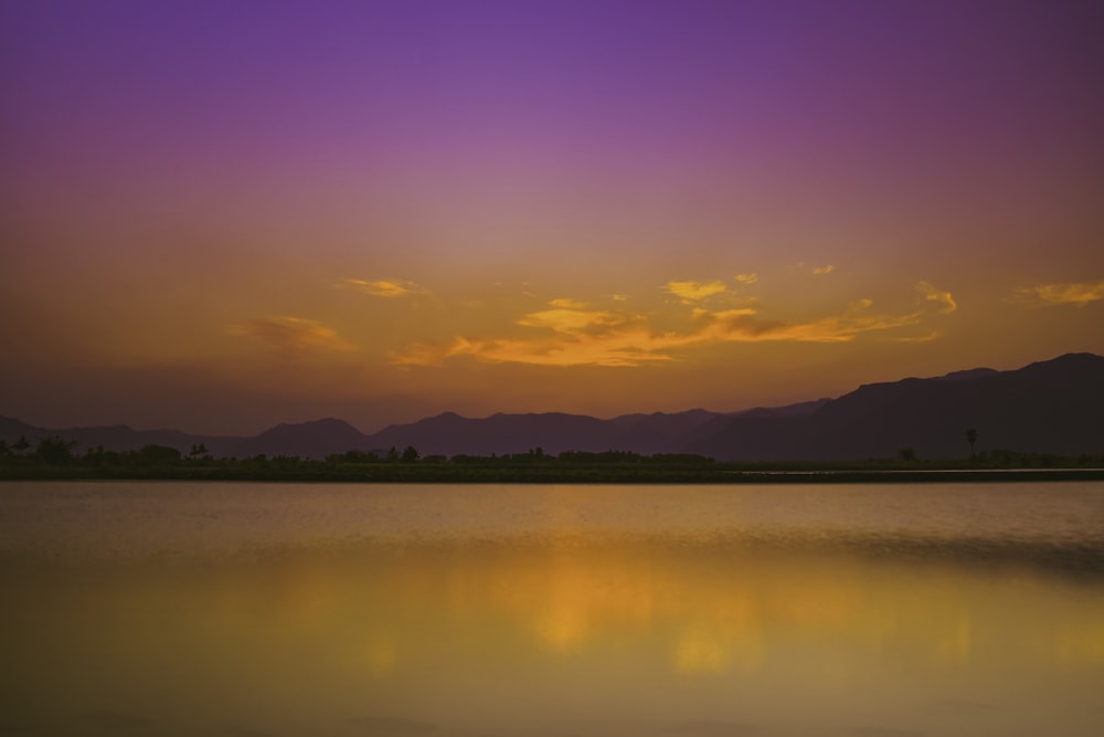 a sunset over a lake with mountains in the background