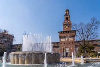 a clock tower towering over a fountain in front of a building