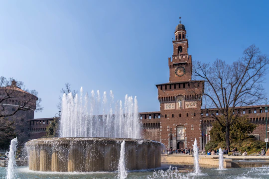 a clock tower towering over a fountain in front of a building