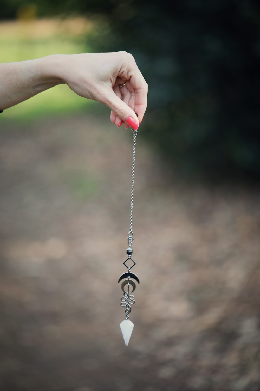 a hand holding a long silver chain with a diamond on it
