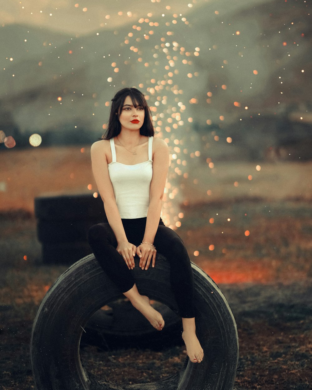 a woman sitting on top of a tire in a field