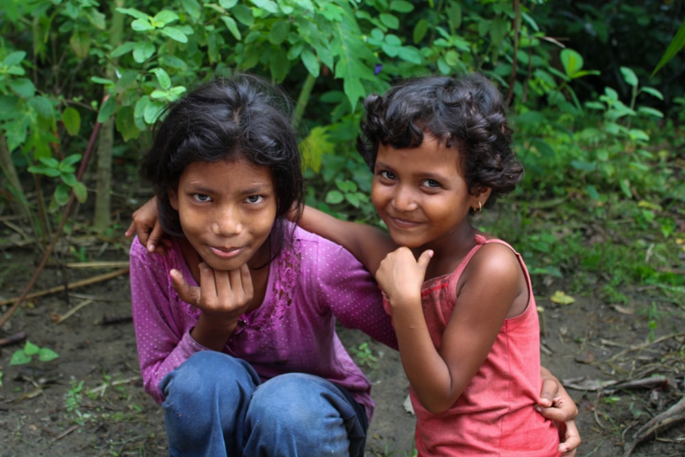 two young girls pose for a picture in front of a bush