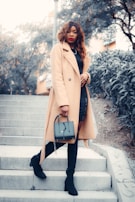 A sunlit street scene featuring a woman in a minimalist camel coat and sleek ankle boots.