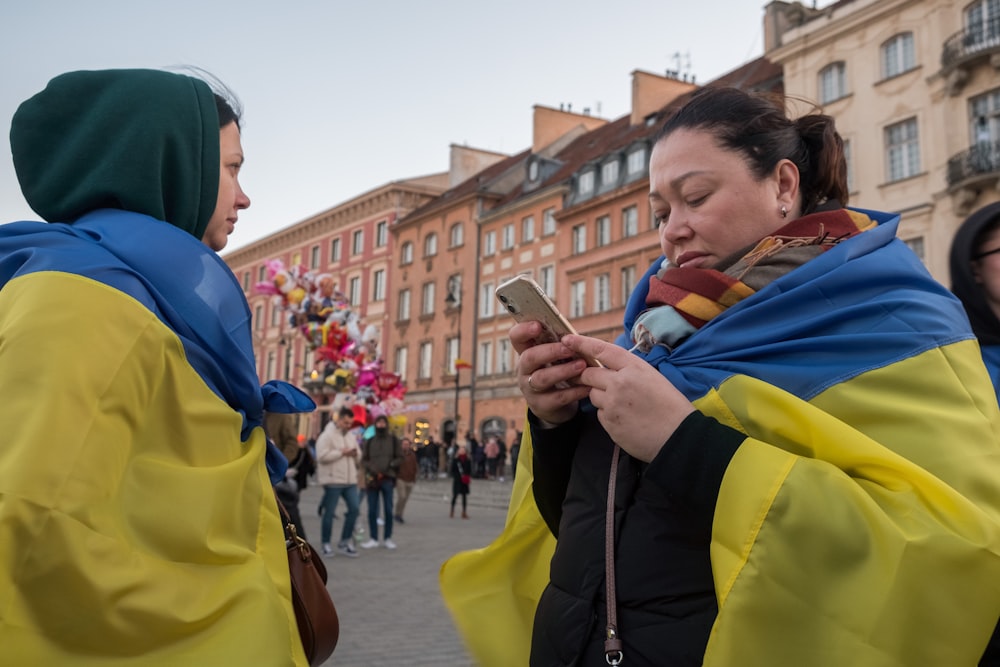 two women standing next to each other looking at a cell phone