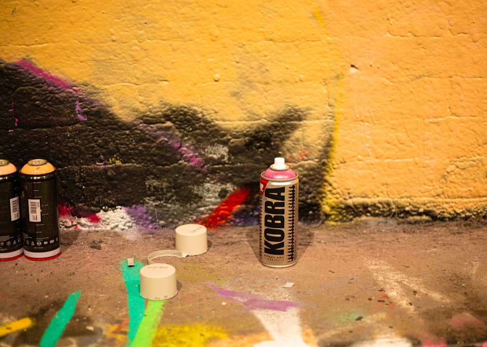 two cans of spray paint next to a wall with graffiti