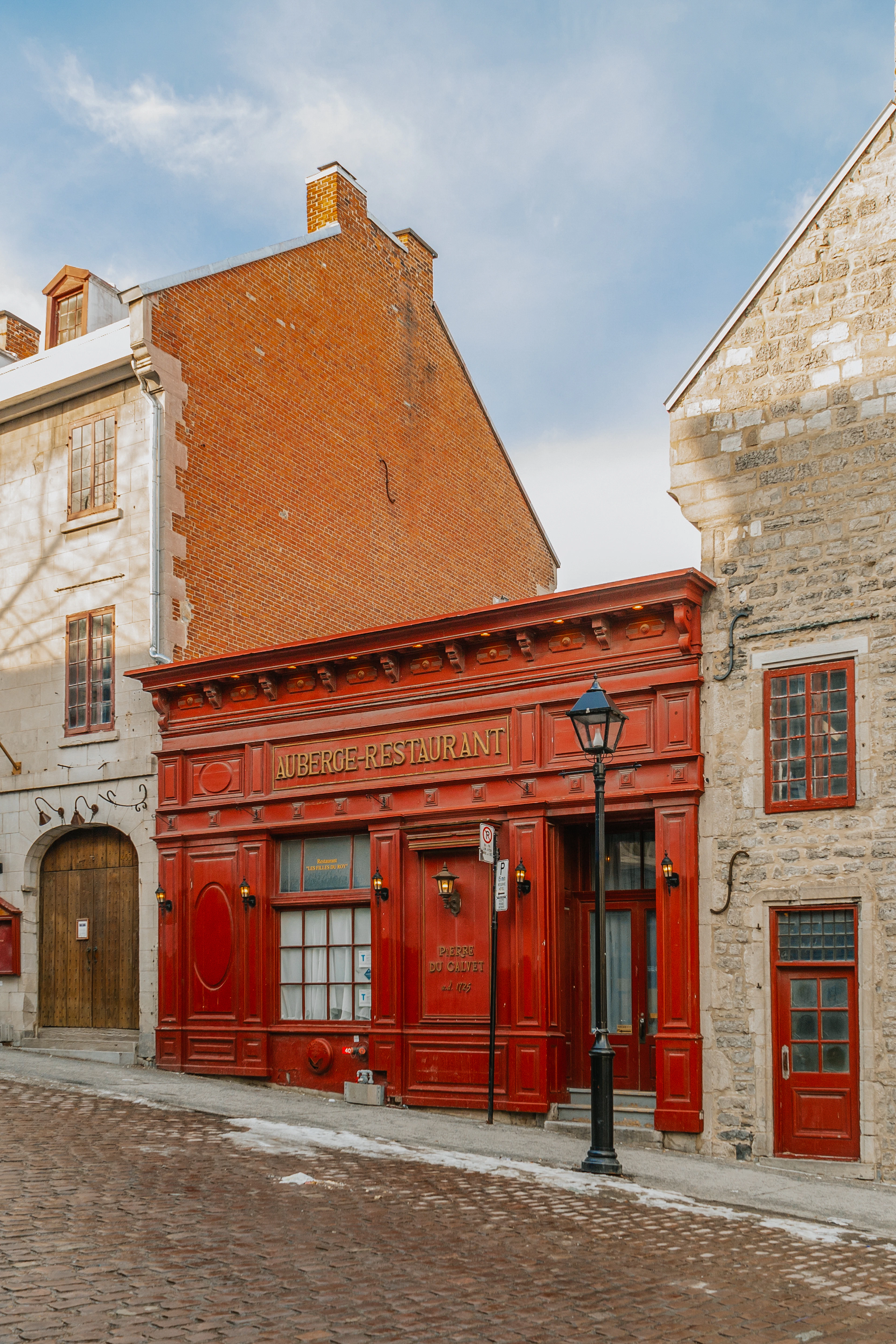 A red-painted 19th-century restaurant facade lines a snowy cobblestone street in Old Montreal.