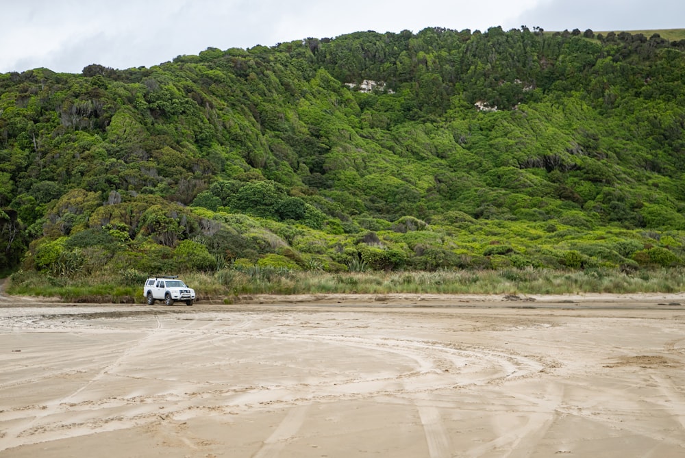 a truck is parked on the beach near a mountain