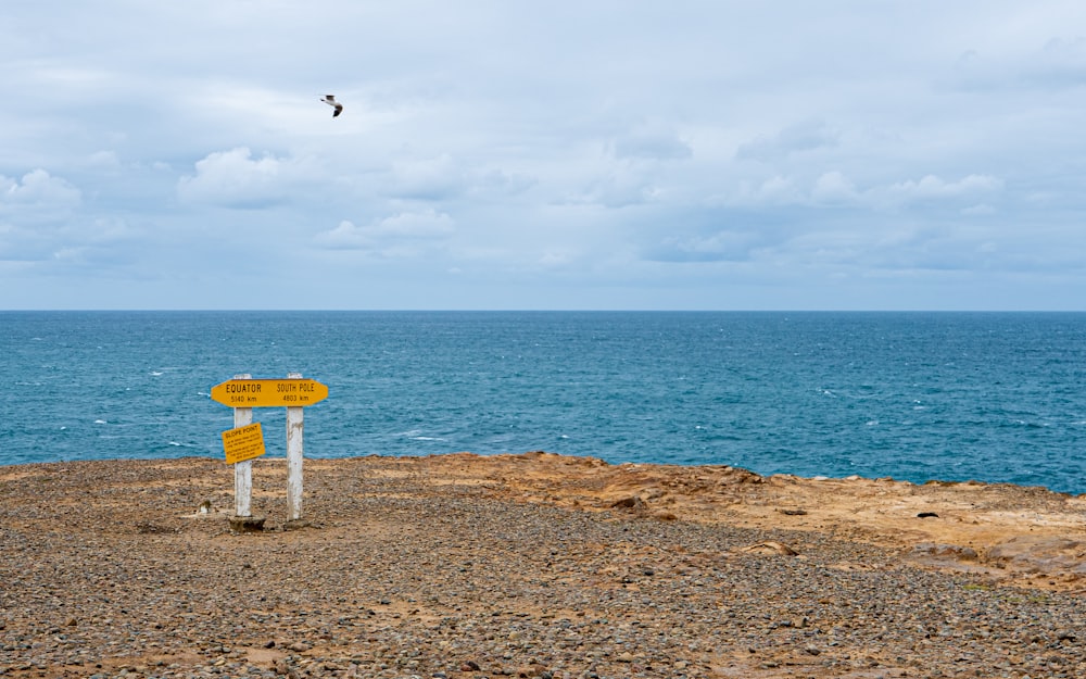 un panneau jaune assis au sommet d’une plage rocheuse
