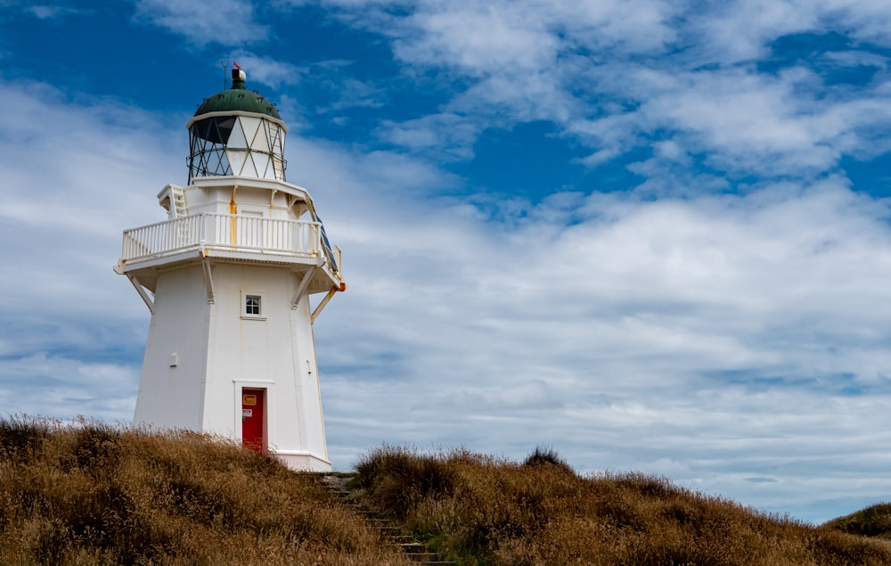 a white lighthouse on a grassy hill under a cloudy blue sky
