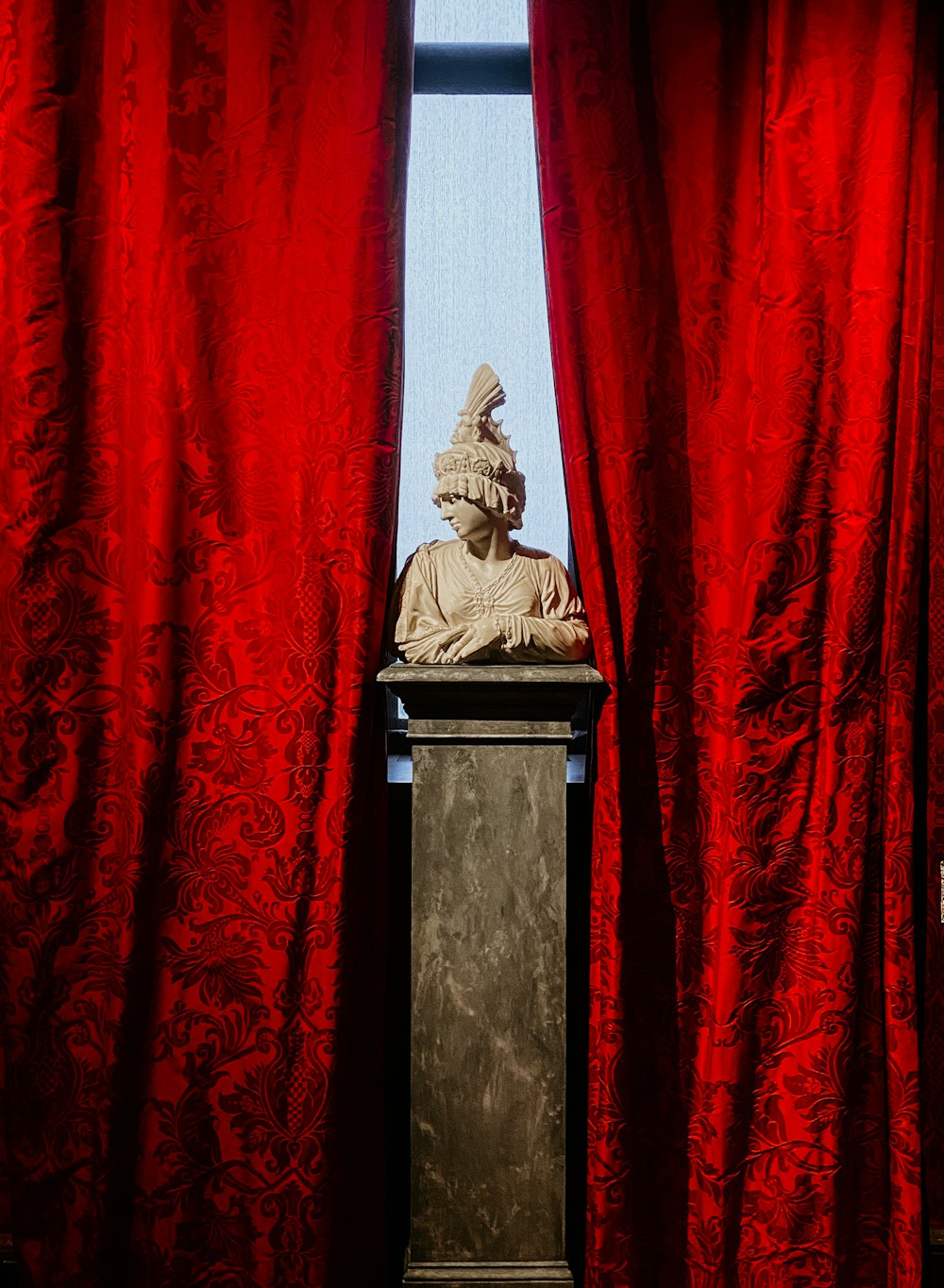 a statue sitting on top of a podium in front of a red curtain