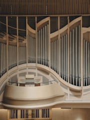 An elaborate and large pipe organ with a curving design, showcasing numerous vertical pipes arranged in an artistic and symmetrical pattern. The organ is set within a wooden structure, emphasizing its grandeur and craftsmanship.