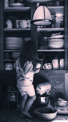 a little girl standing in front of a shelf filled with dishes