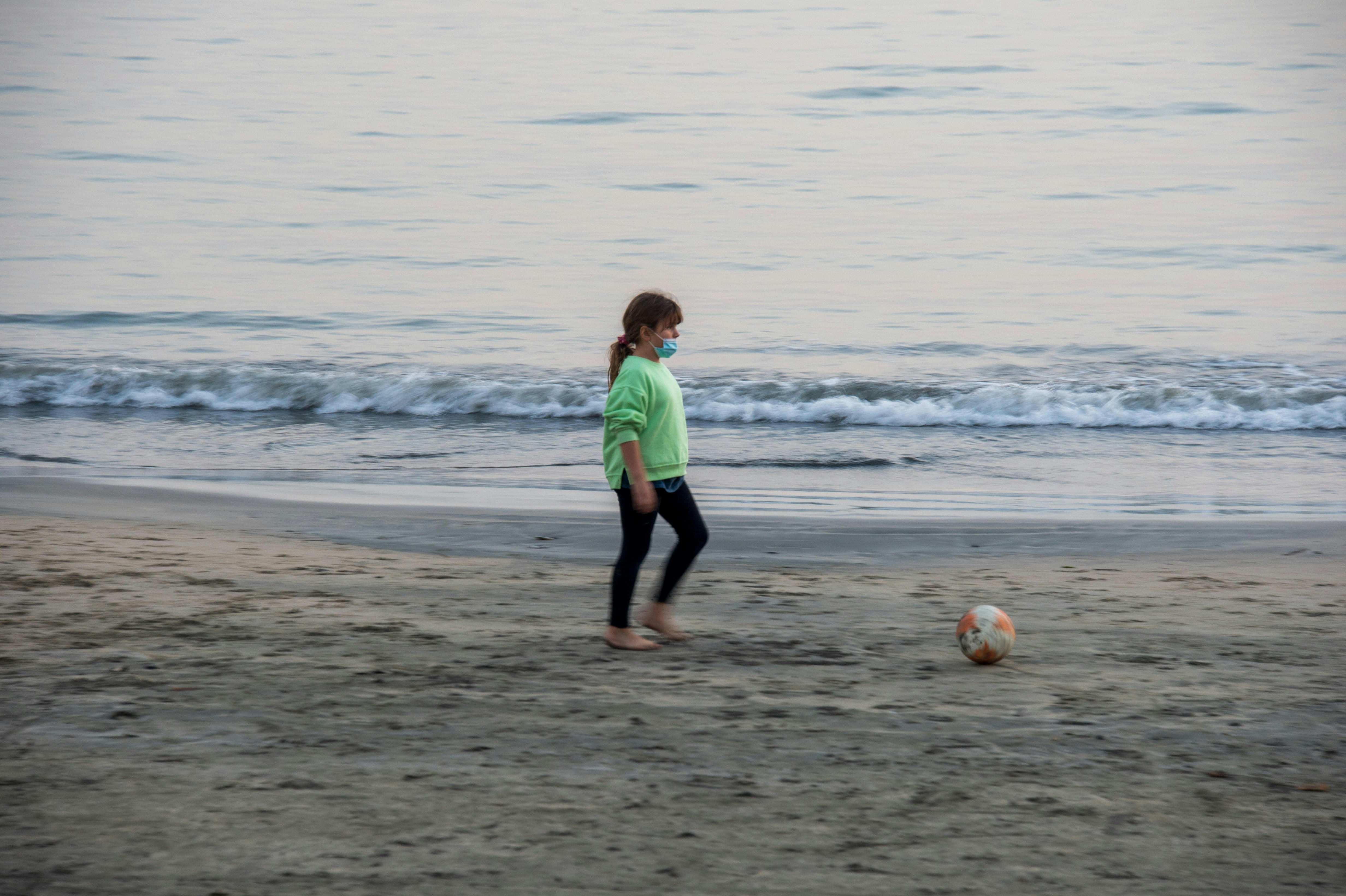 a little girl playing with a soccer ball on the beach