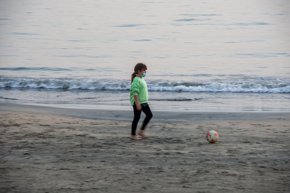 a little girl playing with a soccer ball on the beach
