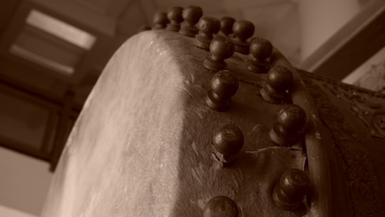 A close-up view of a traditional drum showing the textured surface and large wooden pegs that secure the drumhead. The angle captures the intricate details of the craftsmanship with a sepia-toned effect highlighting the aged appearance.