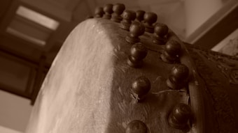 A close-up view of a traditional drum showing the textured surface and large wooden pegs that secure the drumhead. The angle captures the intricate details of the craftsmanship with a sepia-toned effect highlighting the aged appearance.