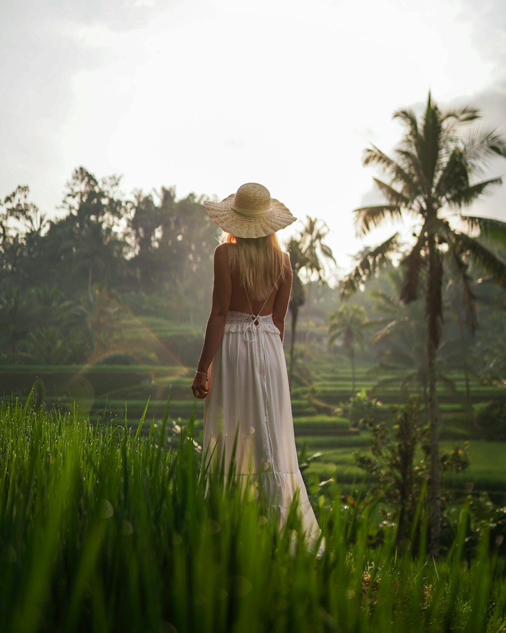 a woman in a white dress and straw hat walking through a field