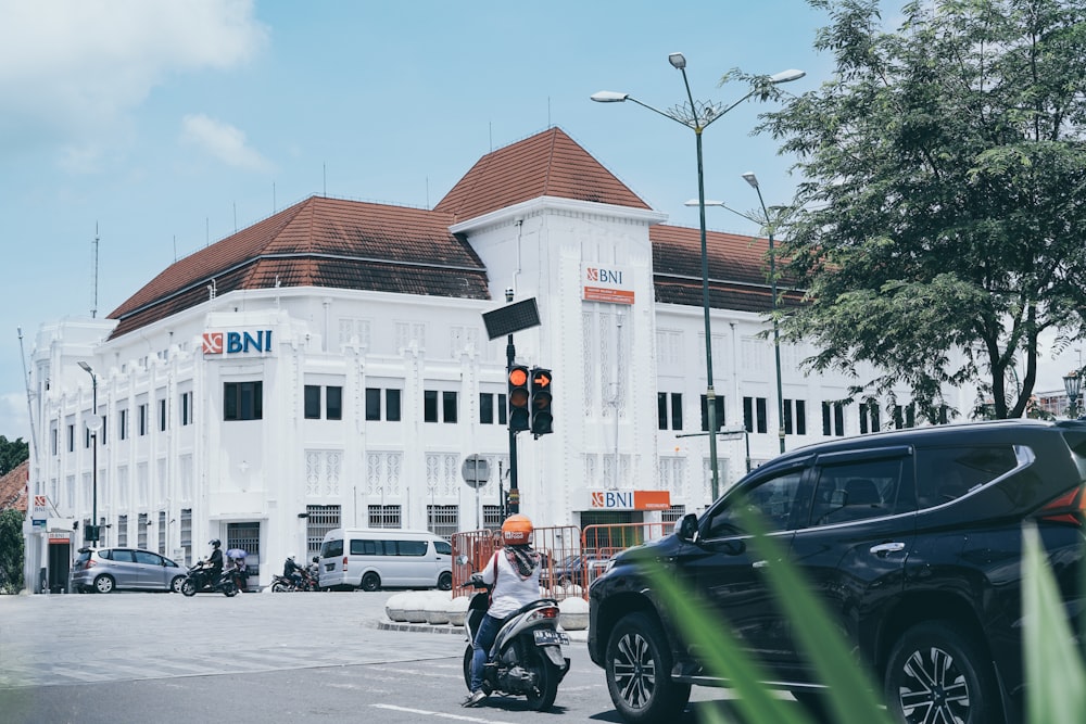 a man riding a motorcycle down a street next to a tall white building