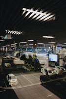 A modern airport scene shows a parked airplane with ground service vehicles nearby. The setting appears to be nighttime with the interior airport lights reflecting on a large glass window, adding depth and complexity to the image.