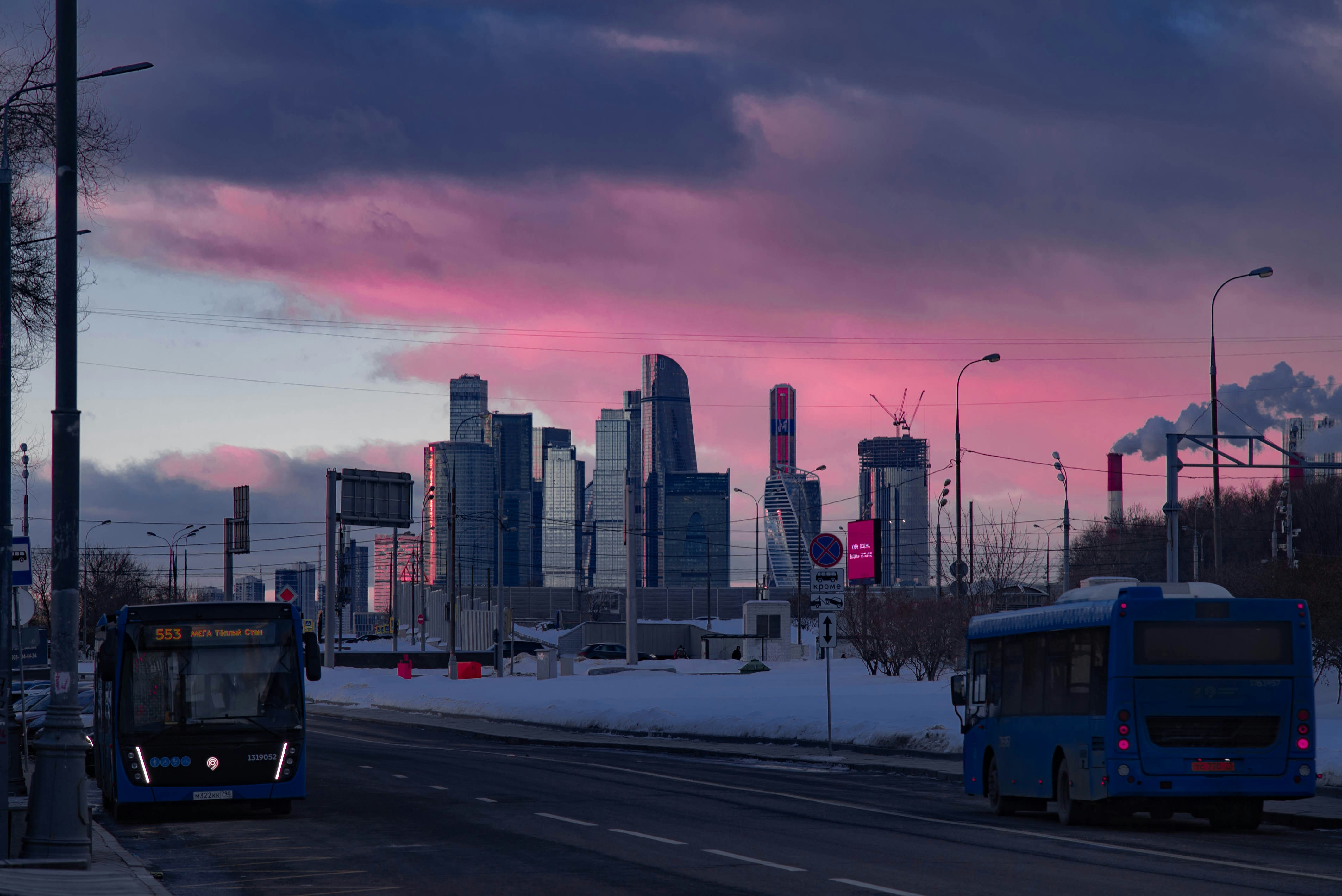 two buses driving down a street with a city in the background