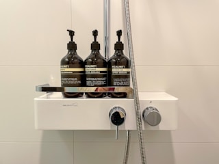 A modern shower rack holding shampoo and soap bottles in a clean shower area.