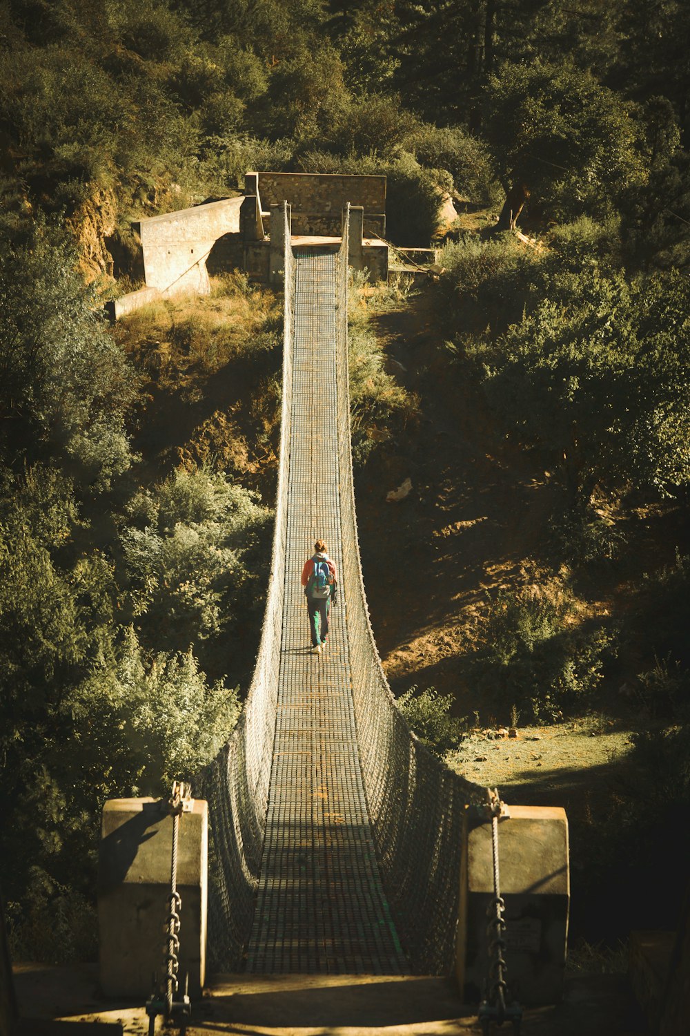 a man walking across a suspension bridge over a river