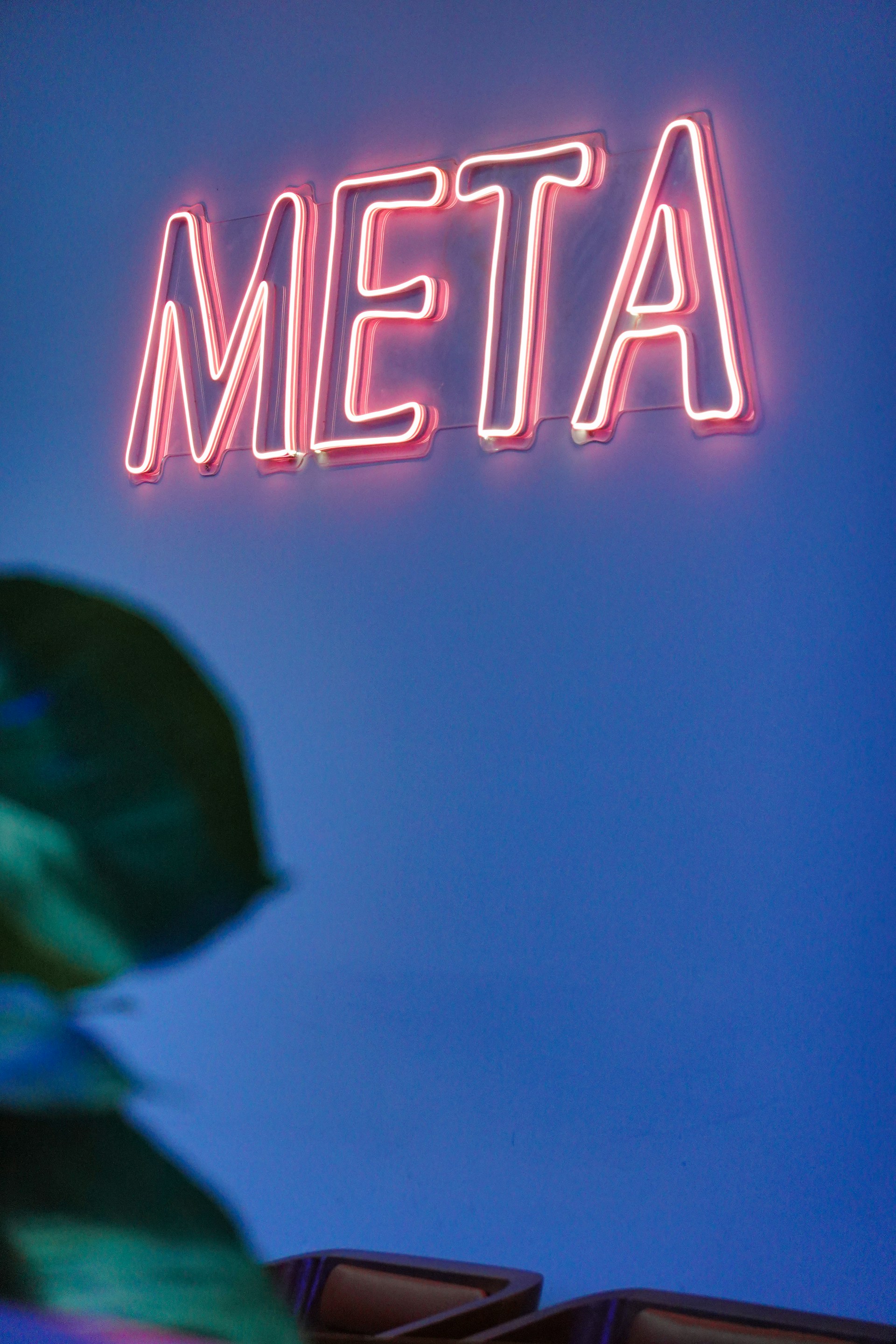 a neon sign that reads meta above a plant