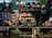 A dimly lit candy and chocolate shop with a variety of sweets displayed on shelves and counters. The shelves are filled with packaged chocolates and candies, some with colorful wrappings and labels. Decorative items like Easter eggs and rabbit figurines are present, along with price tags. Products are arranged neatly, with larger wrapped items like gift packs visible. Overhead lighting casts a warm ambiance over the assortment of confections.