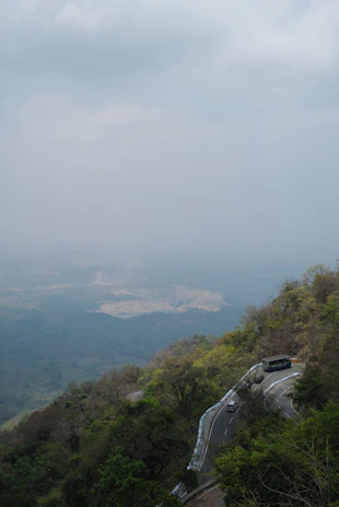 A shuttle driving along a lush green mountain road with mist rolling over the hills.