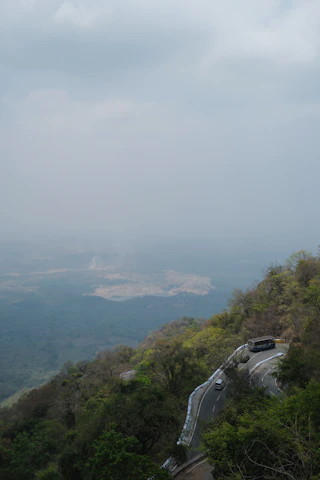 A scenic view of a winding mountain road with a small tour bus driving through lush greenery under a clear blue sky.