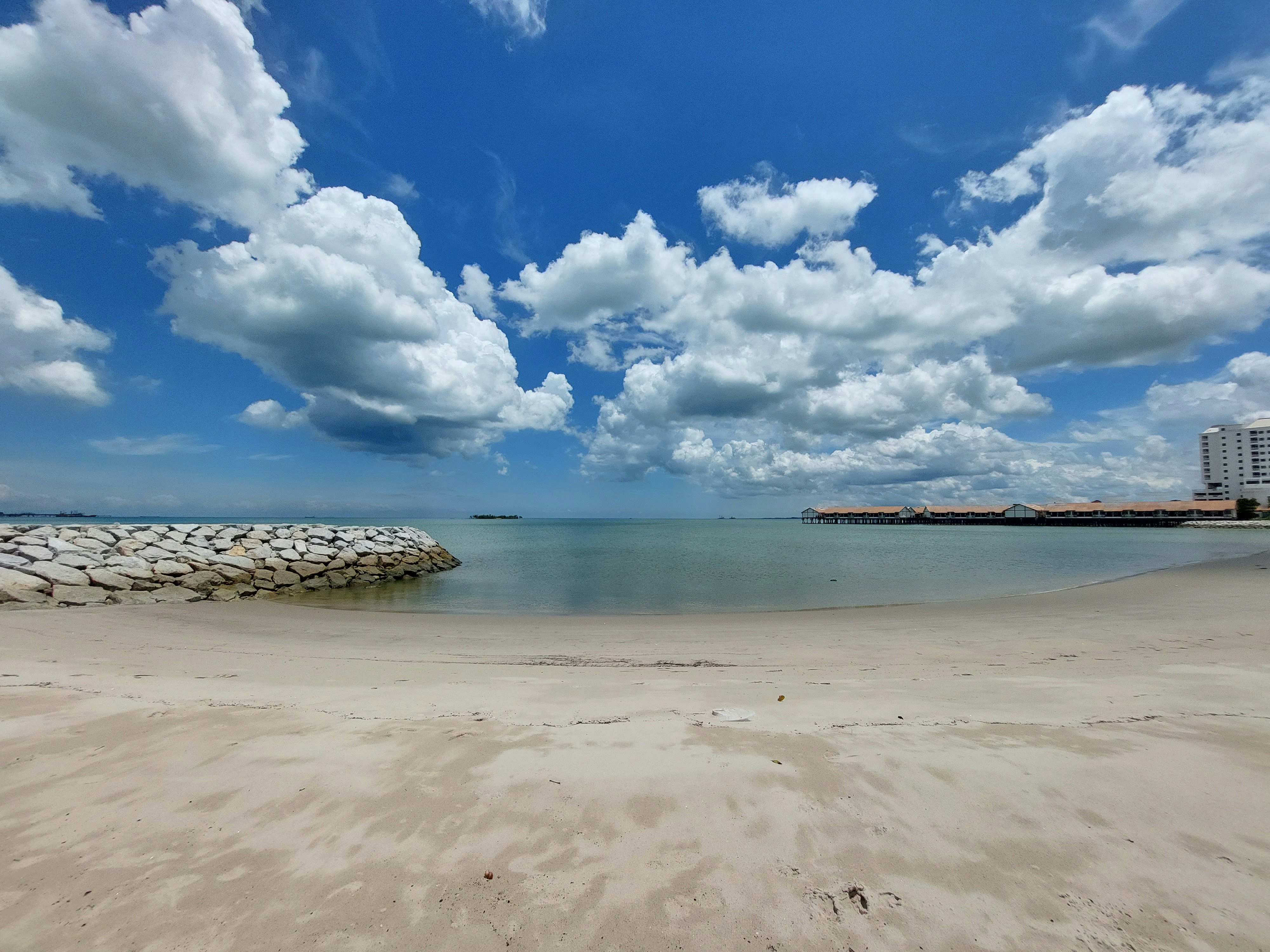 a sandy beach next to the ocean under a cloudy blue sky