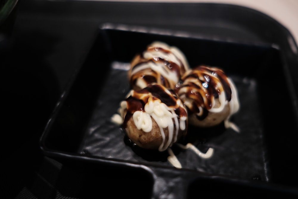 Una bandeja negra cubierta con tres rosquillas cubiertas de chocolate