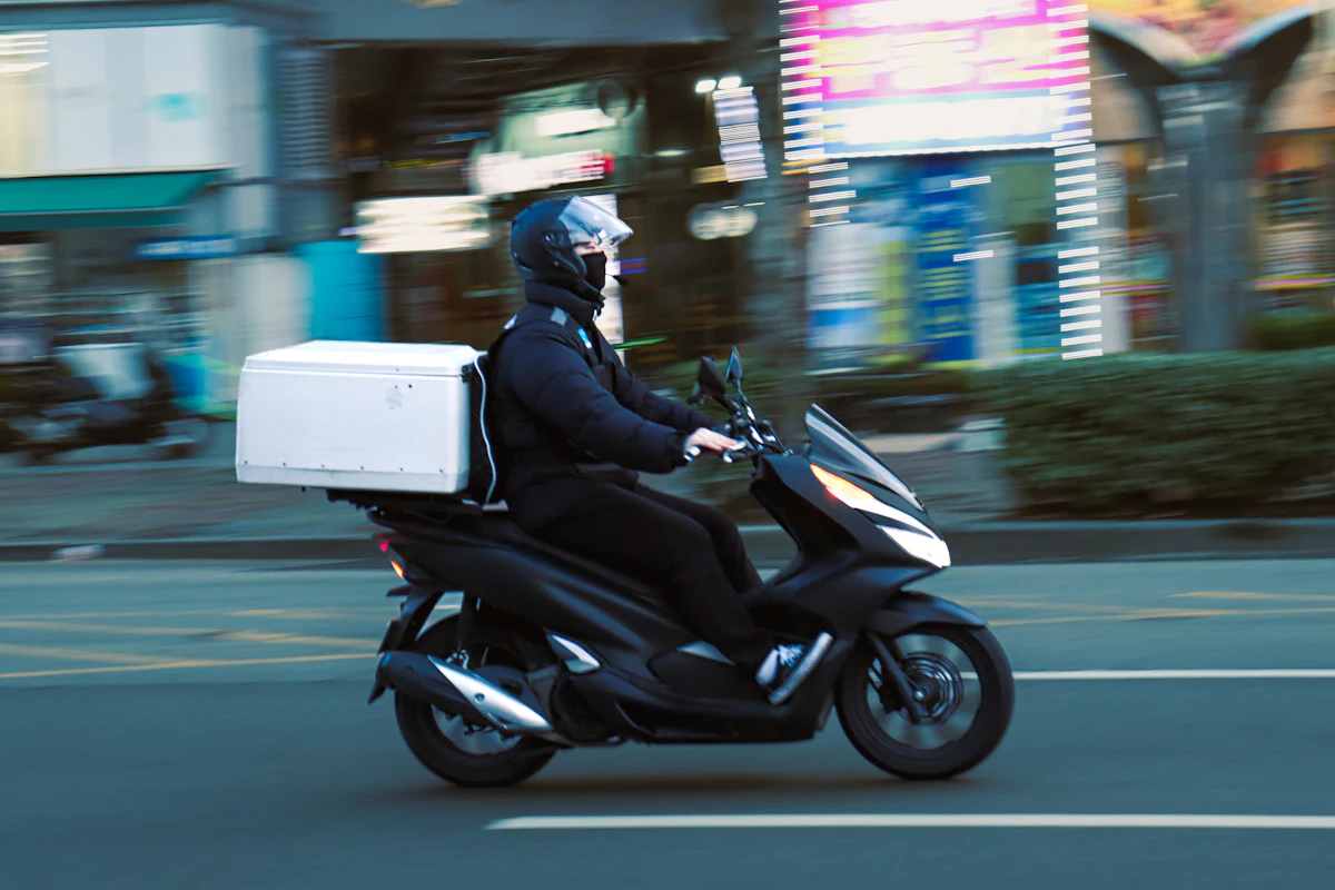 A delivery rider on a scooter with a food box on the back, riding through the city