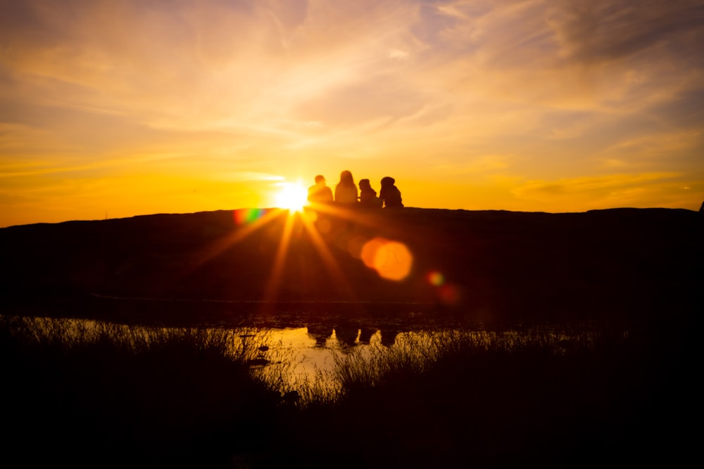 a group of people sitting on top of a hill at sunset