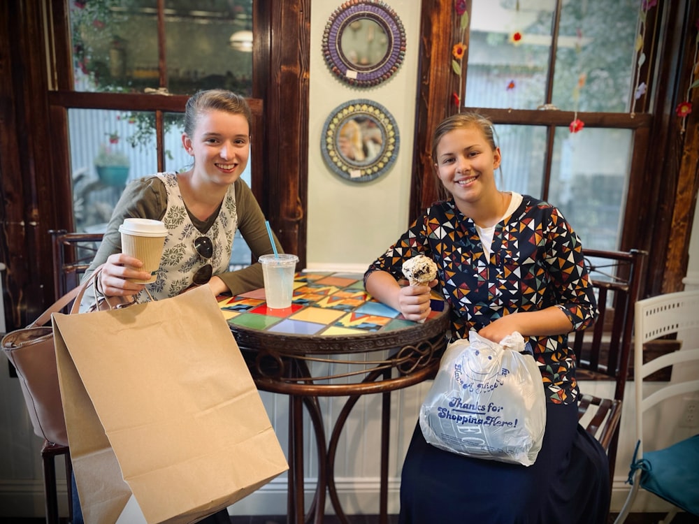 um casal de mulheres sentadas em uma mesa com sacos de papel