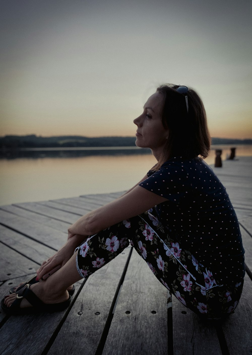 a woman is sitting on a dock at sunset