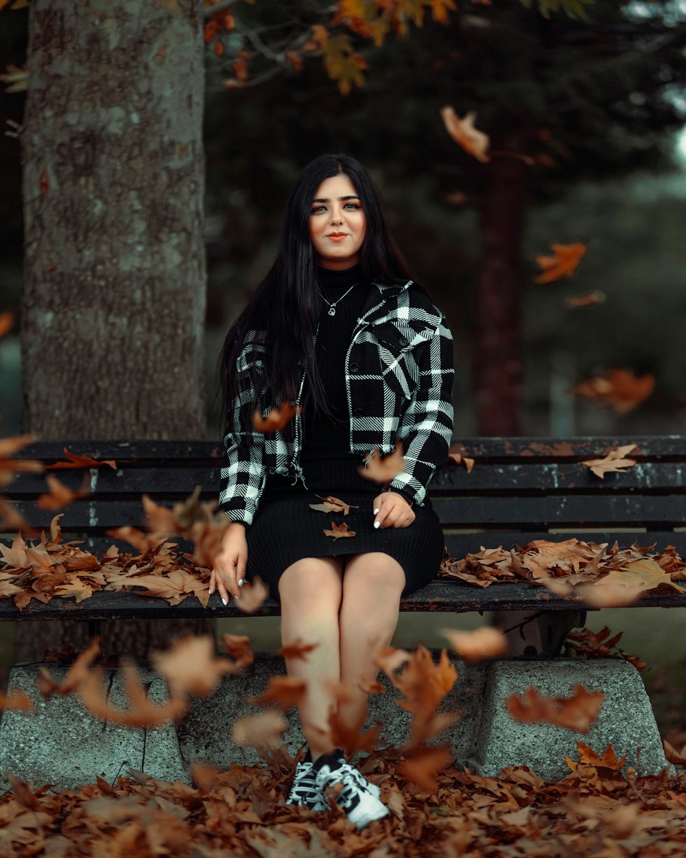 a woman sitting on a park bench surrounded by leaves