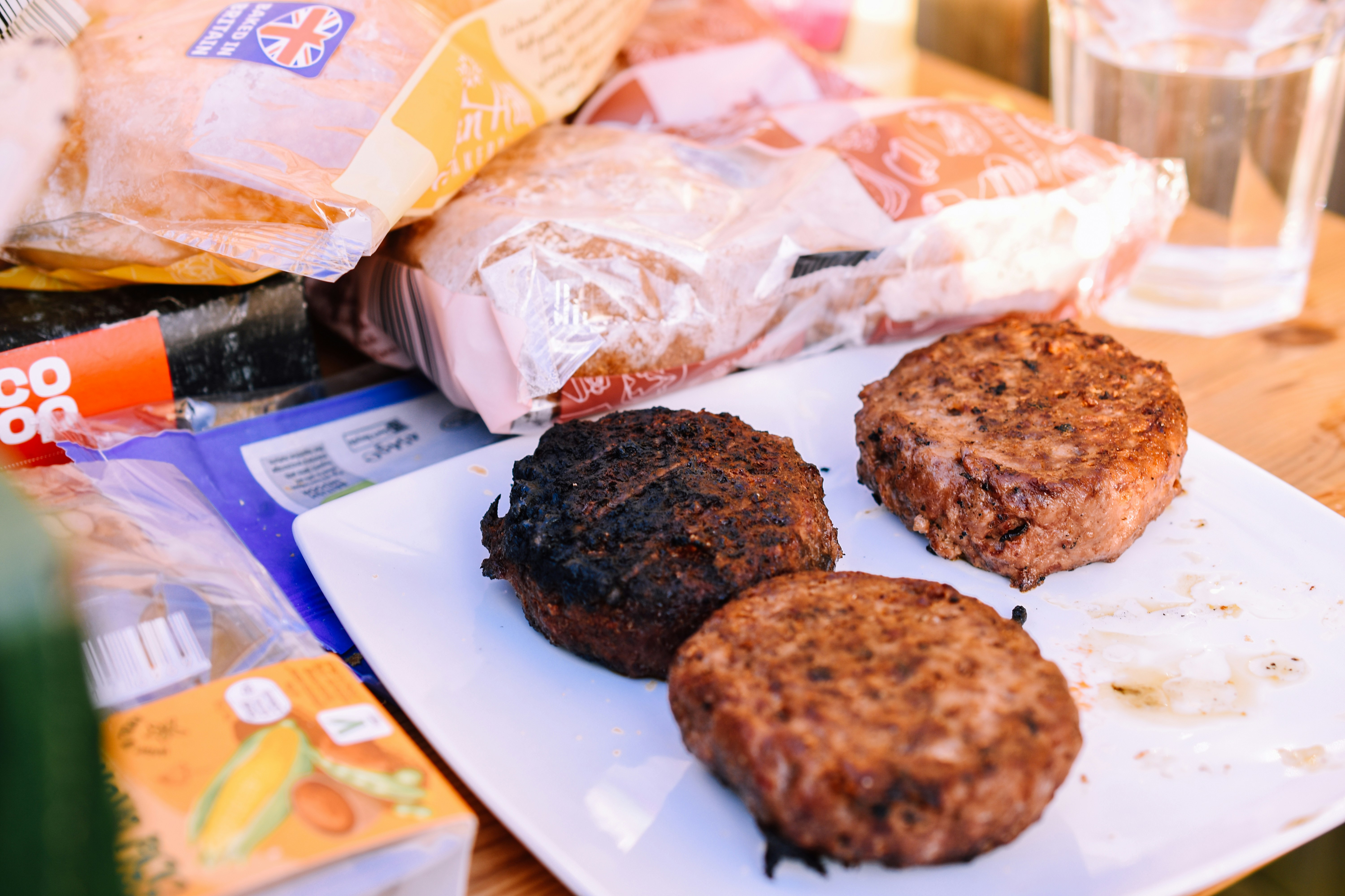 three hamburger patties on a white plate next to a glass of water