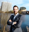 a man in a suit standing in front of a body of water
