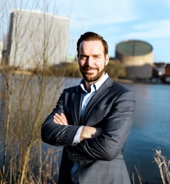 a man in a suit standing in front of a body of water